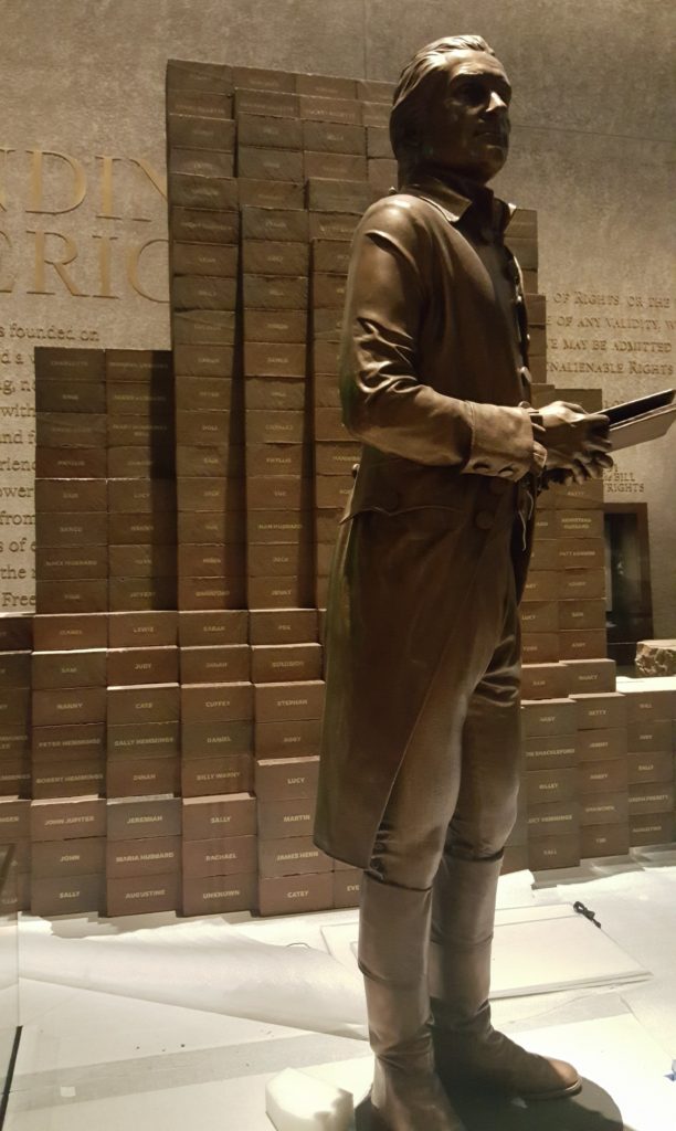 Thomas Jefferson stands in front of a wall dedicated to the Declaration of Independence while each brick behind him represents his slaves.